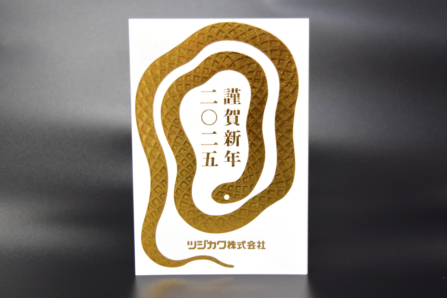 2025年ツジカワ年賀状 ヘビのイラストが箔押しされている
